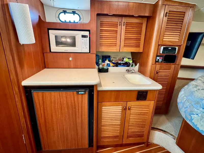 Slide: The Image of 2003 Pursuit 3400 Express boat interior with kitchenette, featuring microwave, sink, and wooden cabinets. - 19