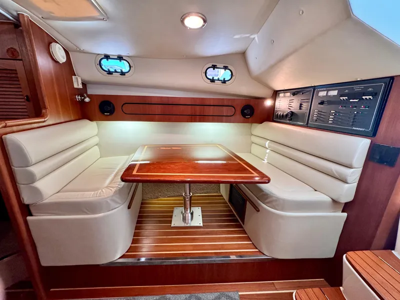 Slide: The Image of 2003 Pursuit 3400 Express cabin interior with wood table, cushioned seating, and control panels. - 22
