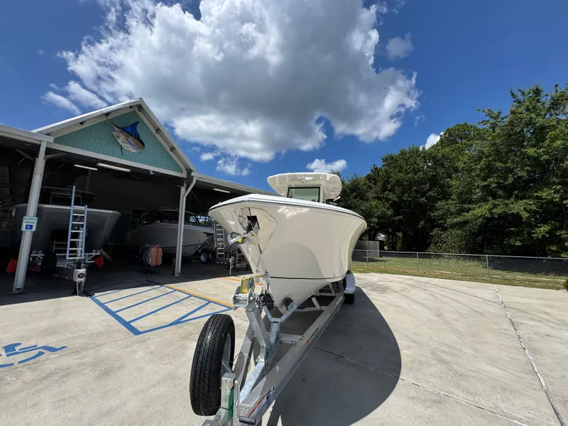 Slide: The Image of 2026 Sailfish 272 CC boat on trailer, parked outside a boathouse under a blue sky. - 6