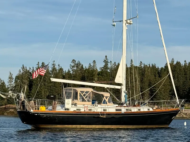 Slide: The Image of Sailboat Bristol 47.7 Cutter/Sloop 1990 on water, forested background, American flag displayed. - 1