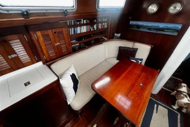 Slide: The Image of Interior of 1990 Bristol 47.7 Cutter/Sloop with wooden table, cushioned seating, and bookshelves. - 3