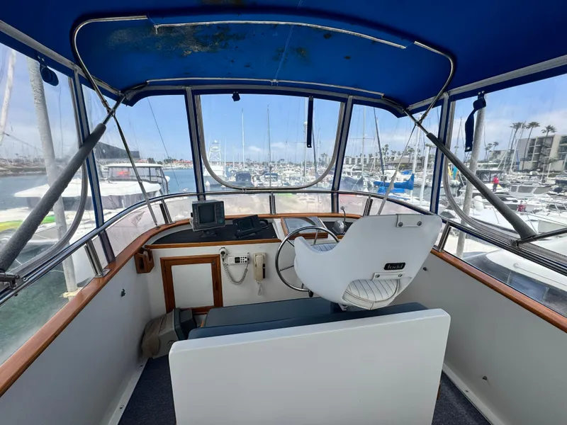 Slide: The Image of 1983 Rough Water Flybridge boat interior with helm, marina view, and blue canopy. - 16