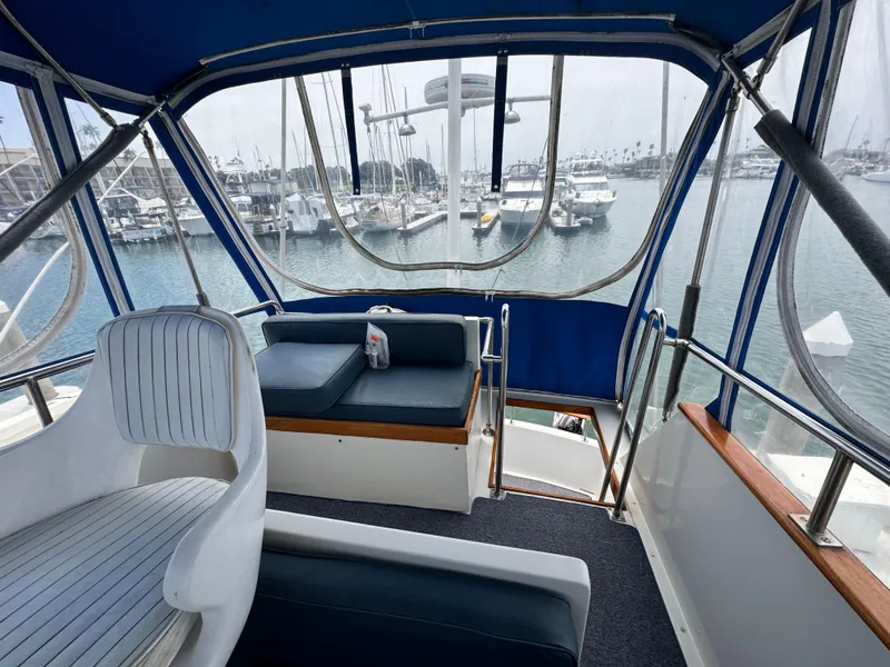 Slide: The Image of 1983 Rough Water Flybridge interior with marina view, featuring blue seating and clear canopy. - 17