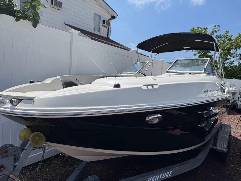 The Image of 2018 Stingray 234 LR boat on trailer, parked near a white fence under cloudy skies. - 0