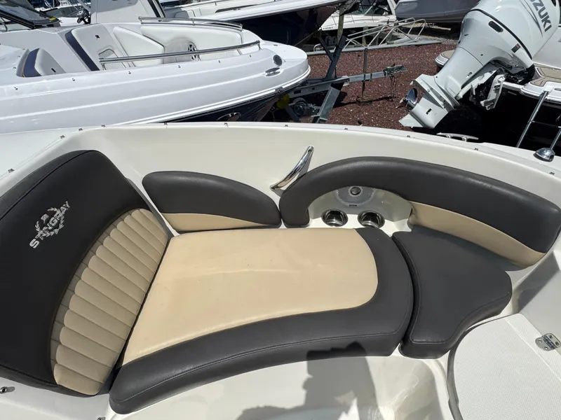 Slide: The Image of 2018 Stingray 234 LR boat interior with beige and black seating, docked near other boats. - 23