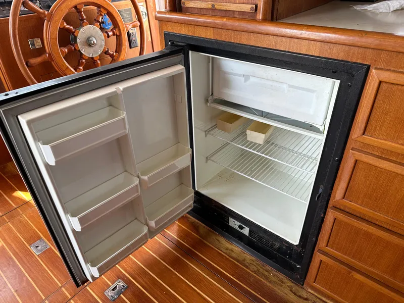 Slide: The Image of Open fridge in 1996 Island Gypsy 36 Aft Cabin boat interior, wooden helm visible. - 42