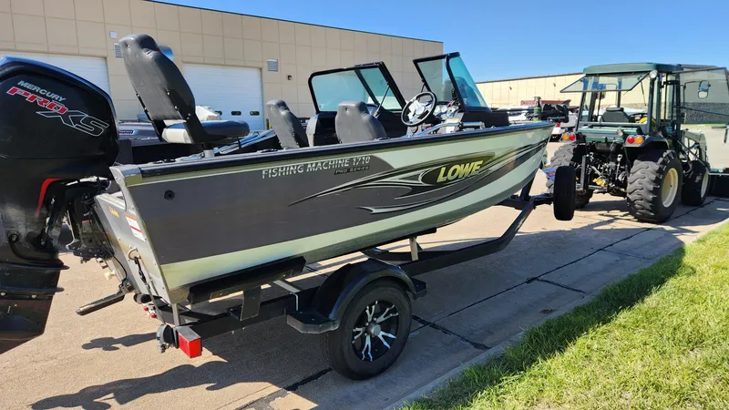 Slide: The Image of 2017 Lowe FM 1710 Pro WT fishing boat on trailer, parked near a tractor. - 12