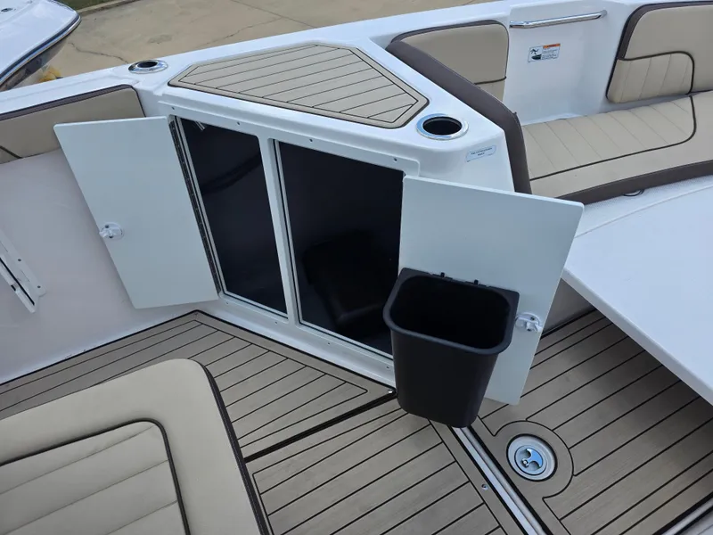 Slide: The Image of 2025 Yamaha Boats 222 FSH Sport E interior with open storage compartment and trash bin. - 6