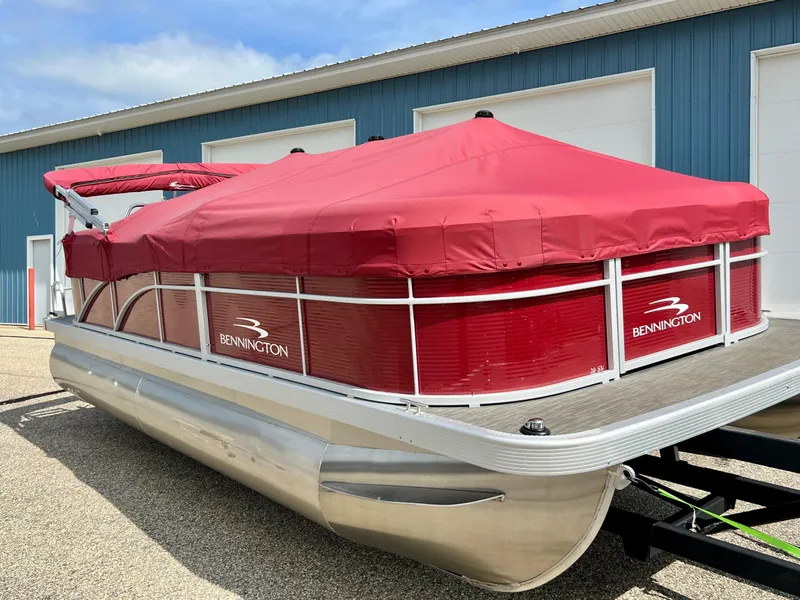 Slide: The Image of 2023 Bennington 20 SVSR pontoon boat with red cover, parked outside a blue building. - 3