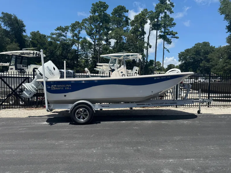 Slide: The Image of 2025 Carolina Skiff 19 LS boat on trailer, parked outdoors with trees in background. - 0