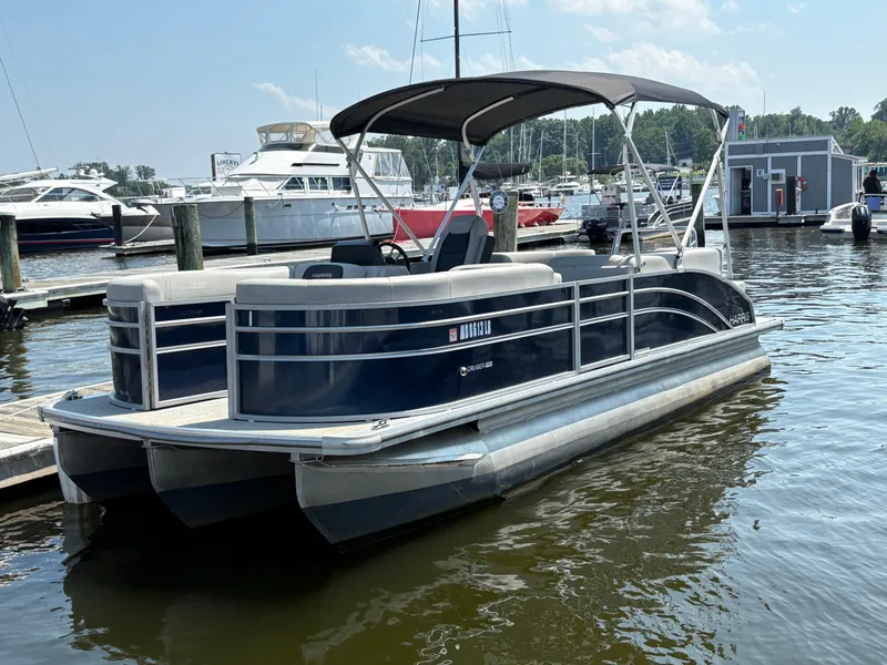 Slide: The Image of 2024 Harris Cruiser 230 pontoon boat docked in a marina, featuring sleek design and canopy. - 1
