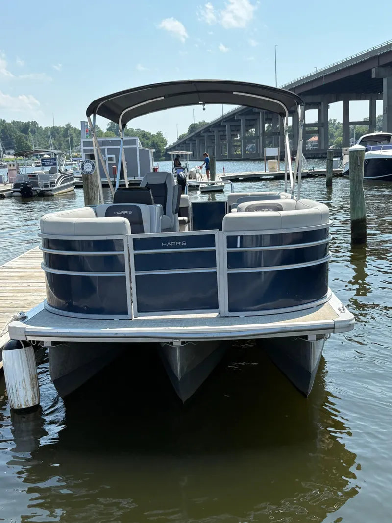 Slide: The Image of 2024 Harris Cruiser 230 pontoon boat docked at marina, under clear sky. - 2