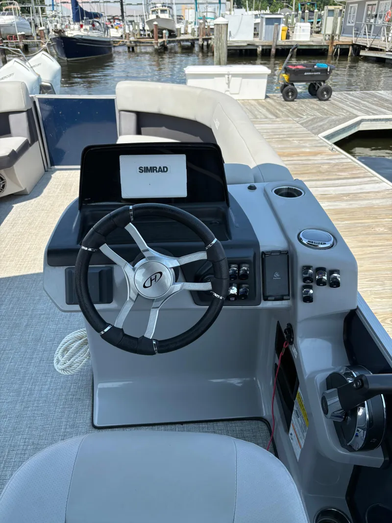 Slide: The Image of 2024 Harris Cruiser 230 boat helm with steering wheel and Simrad display at marina dock. - 6