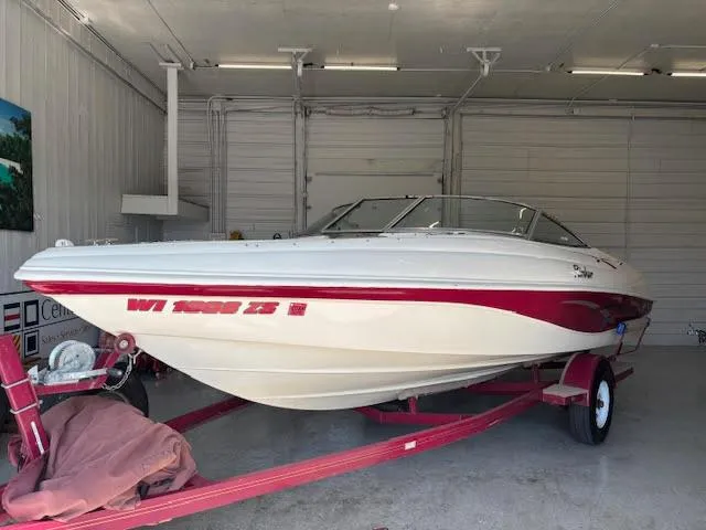 The Image of 2000 Rinker Captiva 212 boat on trailer in garage, white and red design. - 0