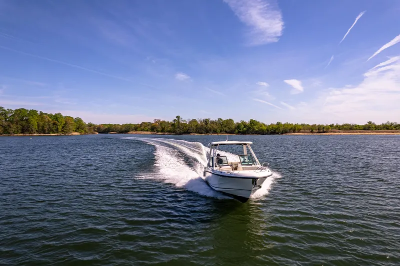 Slide: The Image of 2022 Boston Whaler 240 Vantage cruising on a scenic lake under a clear blue sky. - 10