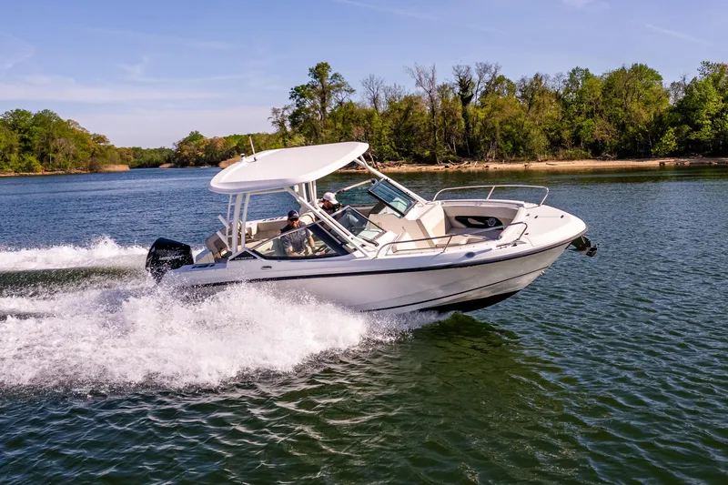 Slide: The Image of 2022 Boston Whaler 240 Vantage cruising on a scenic lake with lush green shoreline. - 12