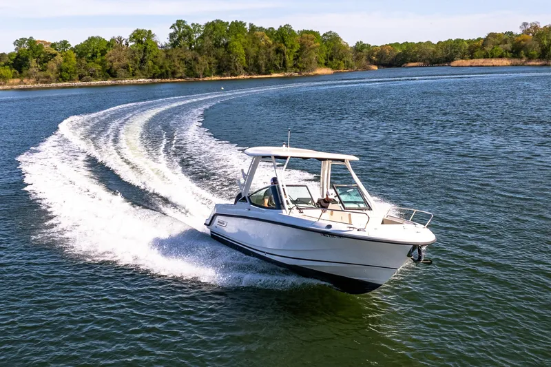 Slide: The Image of 2022 Boston Whaler 240 Vantage cruising on a scenic lake with lush green shoreline. - 8