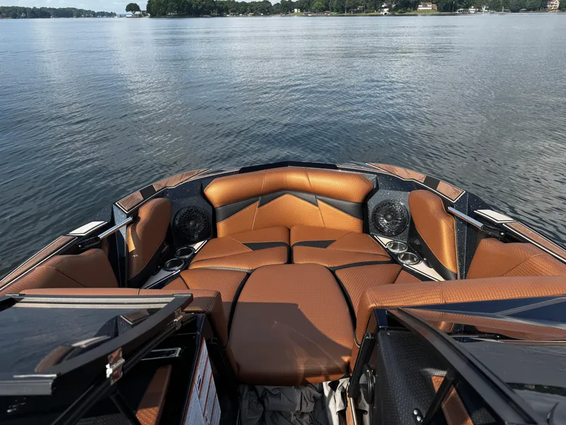 Slide: The Image of 2022 Centurion Fi23 boat interior with brown seating, cup holders, and speakers on a calm lake. - 22