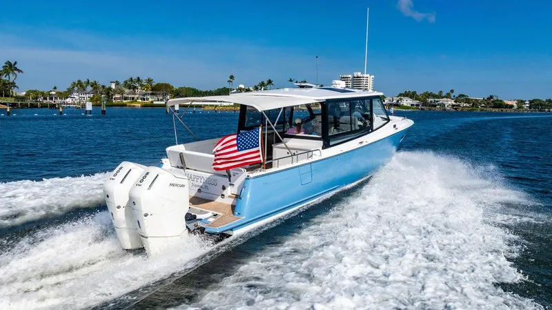 Slide: The Image of 2024 MJM 4 boat cruising on a sunny day with an American flag. - 2