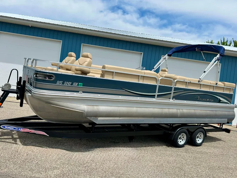 Slide: The Image of 2008 Bennington R25 pontoon boat on trailer, parked near blue building. - 2