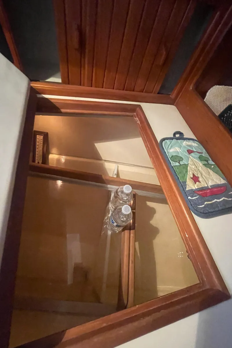 Slide: The Image of Interior of 1995 Island Packet 40 sailboat with open wooden cabinet and water bottles. - 26