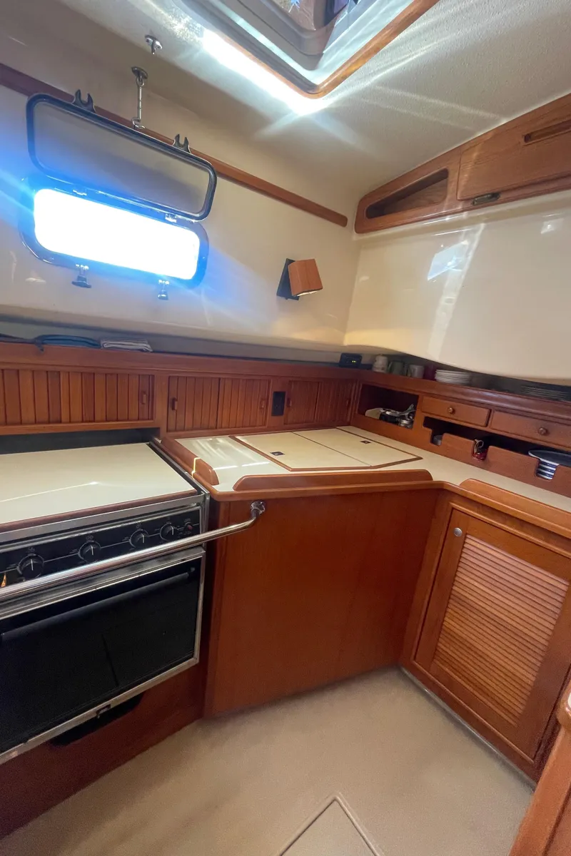 Slide: The Image of 1995 Island Packet 40 yacht kitchen with stove, wooden cabinets, and natural light. - 28