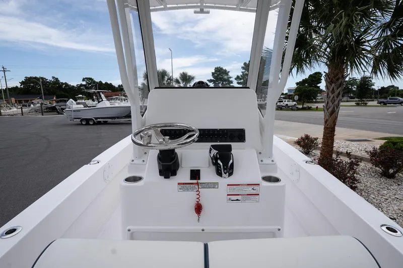 Slide: The Image of 2026 Twin Vee 22 Bay Cat boat console with steering wheel and controls, parked near palm trees. - 10