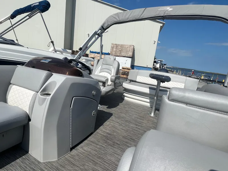 Slide: The Image of 2021 Bennington 23L pontoon boat interior with gray seating and helm, docked under blue sky. - 14