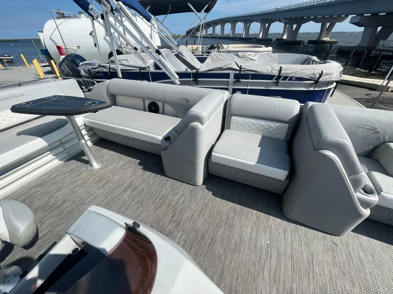 Slide: The Image of 2021 Bennington 23L pontoon boat interior with gray seating and table, docked near a bridge. - 17