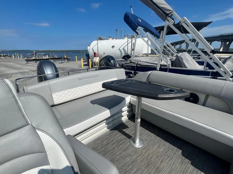 Slide: The Image of 2021 Bennington 23L pontoon boat interior with seating and table, docked by the water. - 20