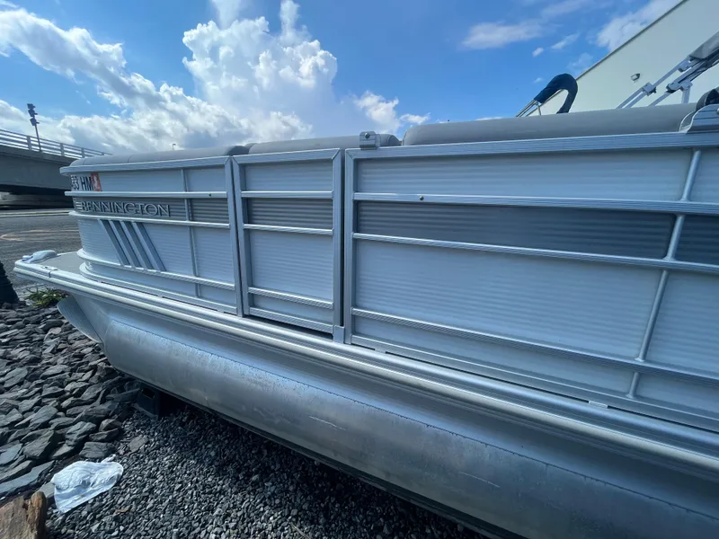 Slide: The Image of 2021 Bennington 23L pontoon boat on rocky shore under blue sky. - 4