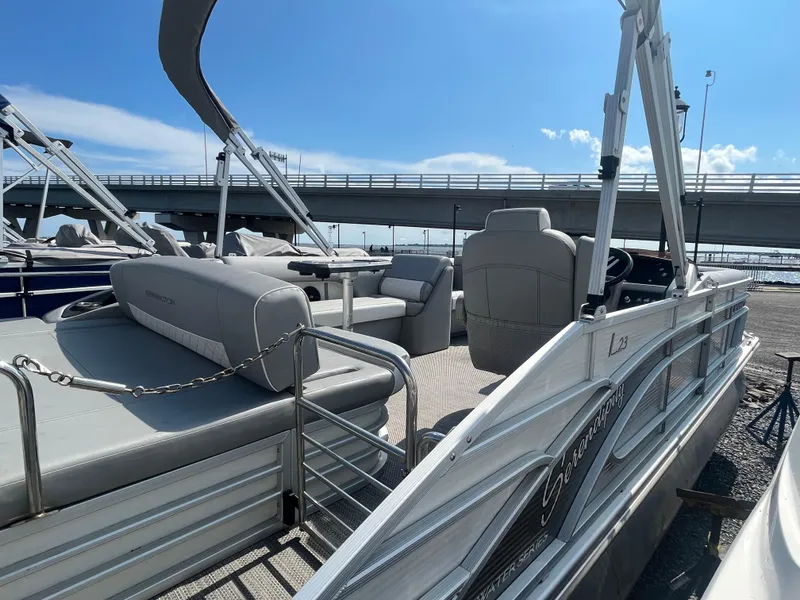 Slide: The Image of 2021 Bennington 23L pontoon boat docked under a bridge, featuring spacious seating and sleek design. - 9