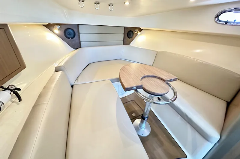 Slide: The Image of 2015 Boston Whaler 315 Conquest cabin interior with beige seating and wooden table. - 29