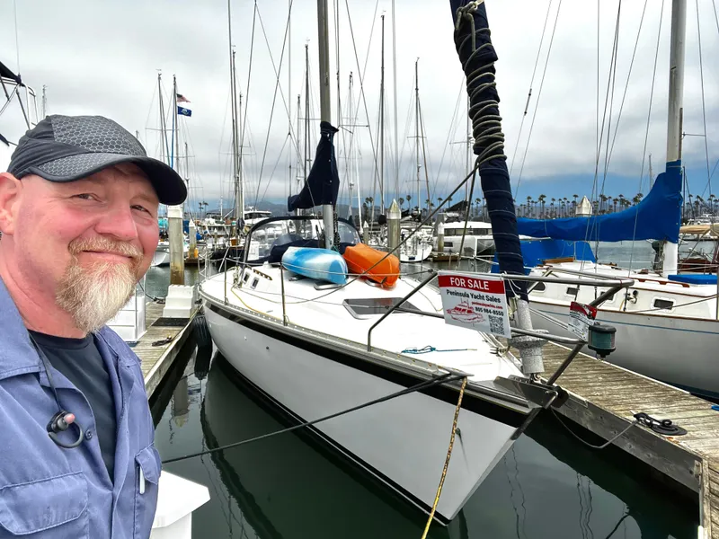 Slide: The Image of Man smiling beside a 1988 Hunter 40 sailboat for sale at a marina. - 5