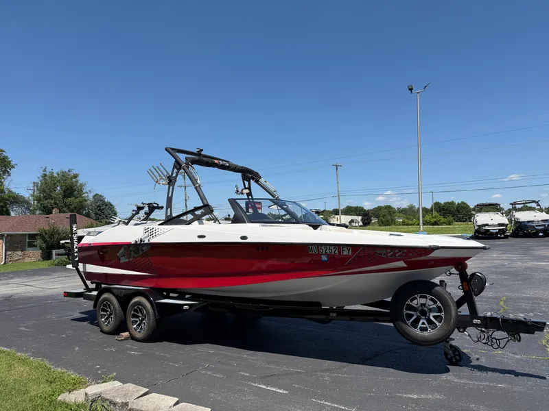 Slide: The Image of 2011 Axis A22 boat on trailer, red and white design, parked outdoors under clear blue sky. - 2