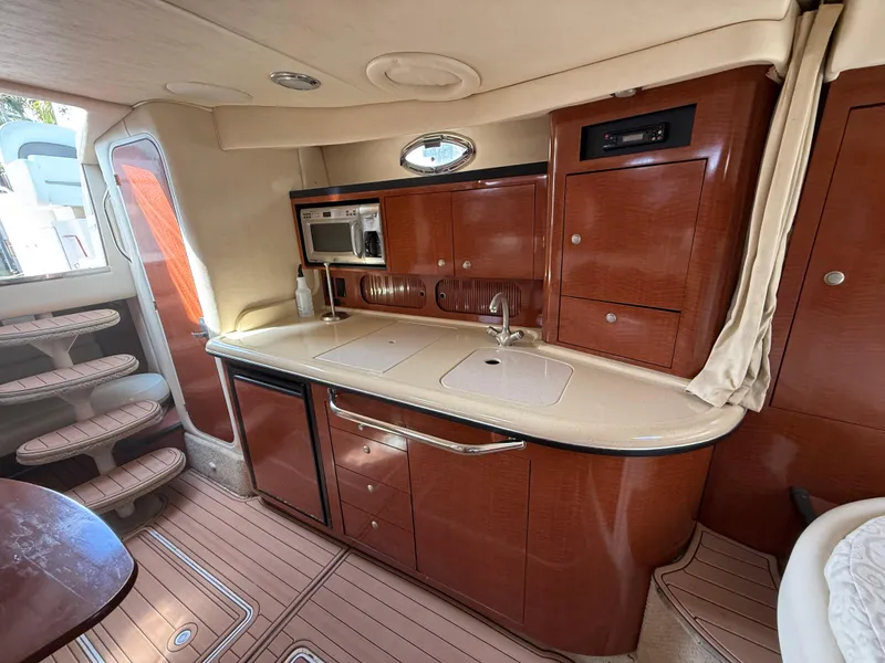 Slide: The Image of 2005 Sea Ray 340 Sundancer interior with kitchenette, featuring wood cabinetry and modern appliances. - 24