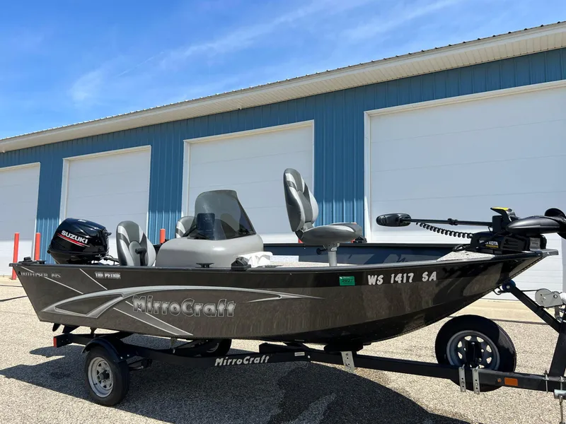 Slide: The Image of 2021 MirroCraft 145 Side Console boat with Suzuki motor, parked outside a blue building. - 13