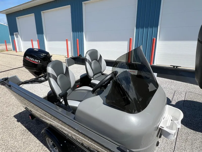 Slide: The Image of 2021 MirroCraft 145 Side Console boat with Suzuki outboard motor, parked near blue building. - 16