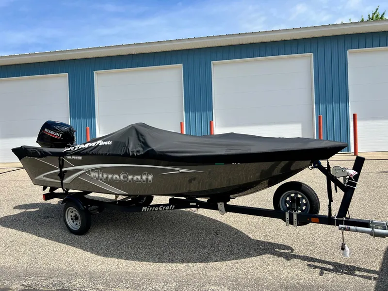 Slide: The Image of 2021 MirroCraft 145 Side Console boat with cover on trailer, parked near blue building. - 2