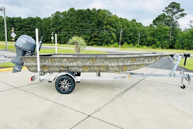 The Image of 2026 War Eagle 648LDV boat on trailer, camo design, Yamaha motor, parked on concrete. - 2