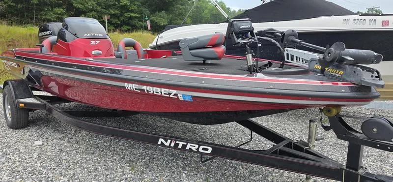 Slide: The Image of 2015 Nitro Z7 boat on trailer, red and black design, parked on gravel. - 0