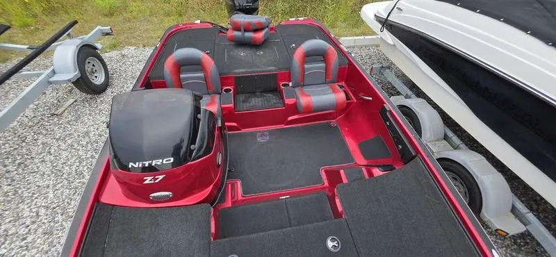Slide: The Image of Red Nitro Z7 boat interior with seating, carpeted floor, and motor, parked beside a trailer. - 7