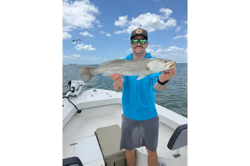 Slide: The Image of Man holding fish on May-Craft 238 Center Console boat, 2026 model, under blue sky. - 56