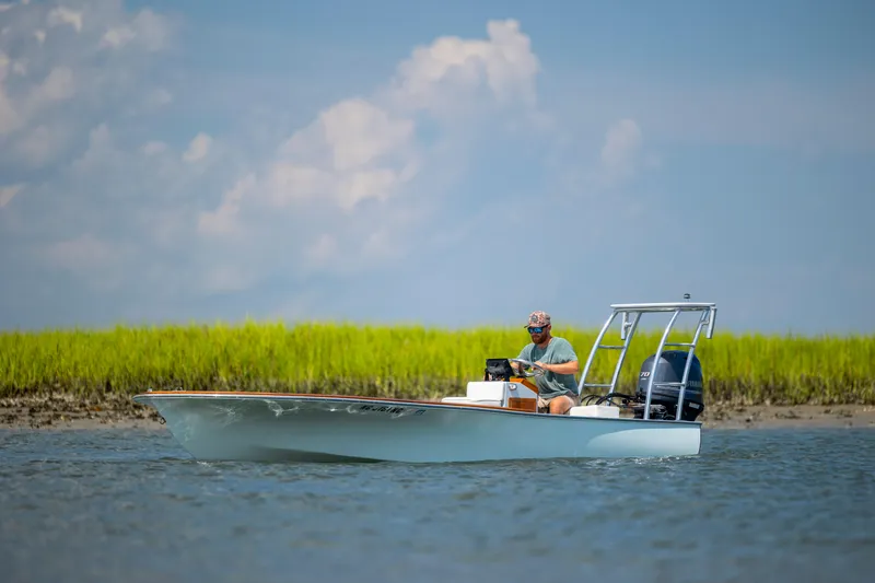 Slide: The Image of 2023 Custom Carolina 18 Flats boat cruising on water with lush green marshland background. - 3