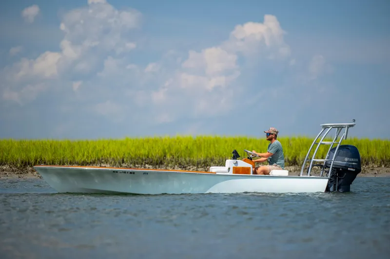 Slide: The Image of 2023 Custom Carolina 18 Flats boat on water with Yamaha engine, grassy shoreline background. - 4