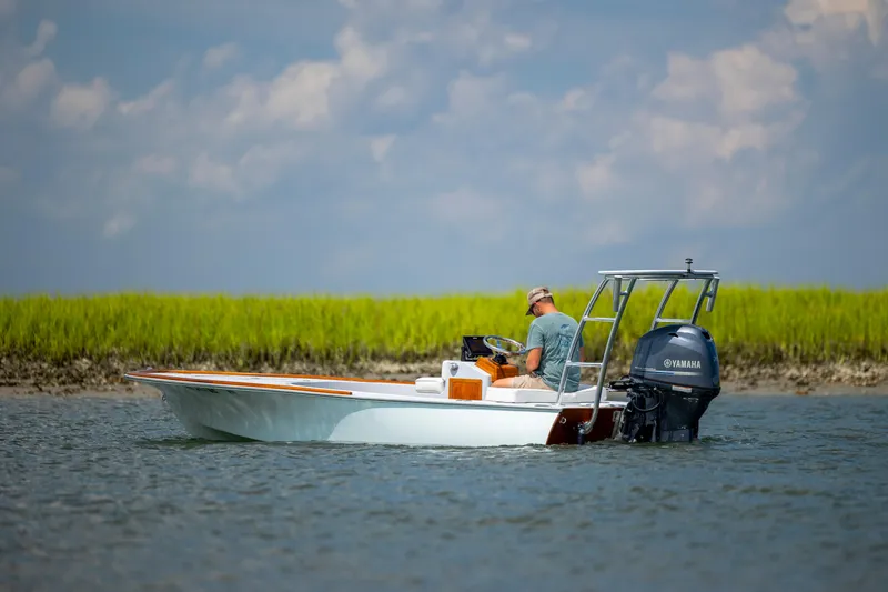 Slide: The Image of Custom Carolina 18 Flats boat navigating shallow waters, 2023 model, with lush green shoreline. - 5