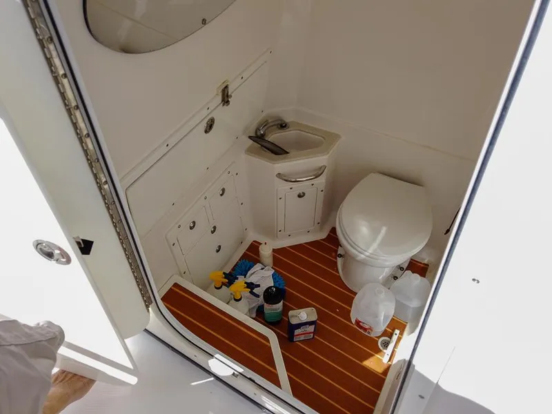 Slide: The Image of 2015 Edgewater 320CC boat bathroom with sink, toilet, and cleaning supplies on wooden floor. - 16