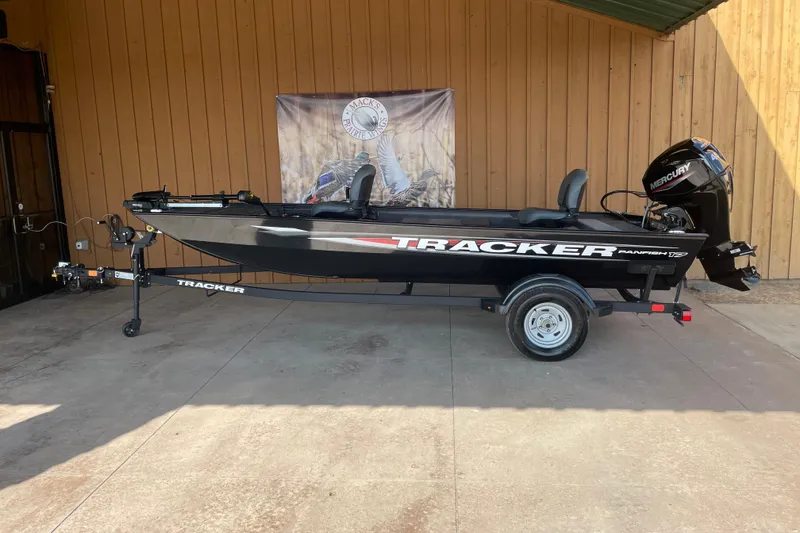 The Image of 2025 Tracker Panfish 17 boat on trailer, displayed outdoors against wooden wall. - 0