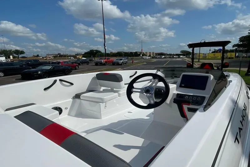 Slide: The Image of 2025 Tahoe T18 boat interior with steering wheel and seating, parked outdoors under a blue sky. - 64