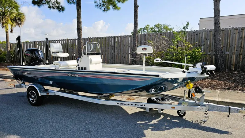 Slide: The Image of 2025 Ranger RB190 boat on trailer, parked outdoors near trees and fence. - 2